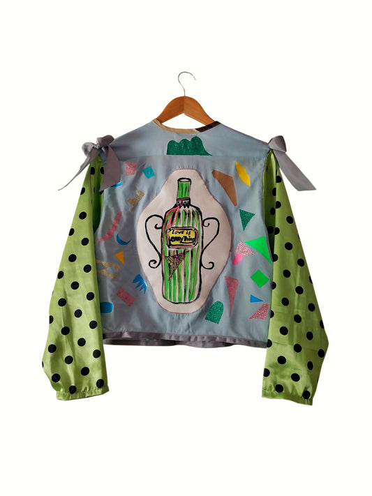 Handmade upcycled cropped pale blue jacket with hand-painted Love Is Everything green bottle centrepiece scattered confetti appliqué and green black polka dot sleeves with grey ribbon shoulder bows