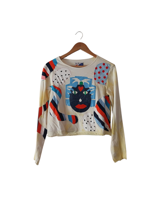 Upcycled crop top with abstract face appliqué, colorful patchwork sleeves, and artistic handmade design on a cream base