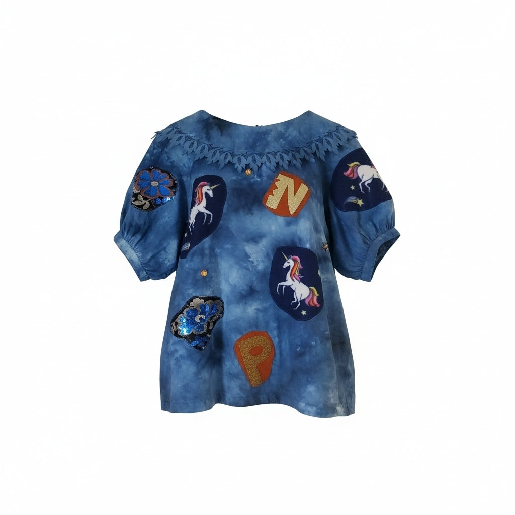 Handmade upcycled tie-dye blue short sleeve shirt with puffed sleeves, lace cut collar and hand-applied unicorn patches varsity letters and sequin flower appliqué